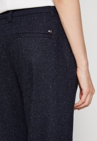 Marinblå texturerade byxor har en figurnära design, med en bakficka och en liten logotypdetalj på midjan.