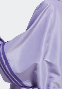 Laventelin satiinivaate, jossa on drapointimuotoilu, ja joka on varustettu tekstuuripinnalla sekä syvän violetilla raidoituksella reunoilla.