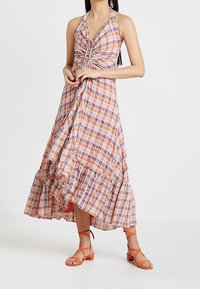 Maxiklänning med halterneck som har en rynkad bodice, flerfärgad rutmönster och en tiered nederkant. Matchad med orangea sandaler med remmar.