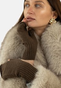 Brązowe bezpalczaste rękawiczki prążkowane wykonane z miękkiego materiału, noszone przez osobę w futrze. Rękawiczki są dopasowane i mają teksturowaną powierzchnię.