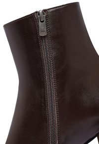 Brown leather ankle boot with a smooth texture, featuring a side zipper and a slightly curved top. Zipper hardware is silver-colored.