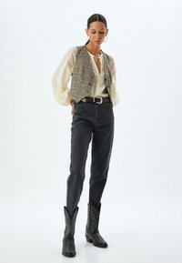 Gevlochten vest over een witte blouse, gecombineerd met hoge donkere jeans en zwarte cowboylaarzen met gegraveerde patronen.