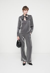 Completo due pezzi grigio metallico composto da una blusa a maniche lunghe con scollatura a V e dettaglio a fiocco, abbinata a pantaloni a gamba larga e una borsa nera.