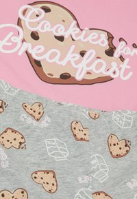Grafický tričko s růžovým pozadím, na kterém je design cookie srdce a bílé písmo "Cookies for Breakfast". Šedý spodní díl s vzory cookies.