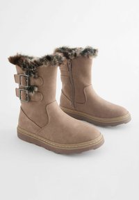 Botas de tobillo de ante sintético marrón con borde de pelaje, dos hebillas en el lateral, cierre de cremallera y suela texturizada para agarre.