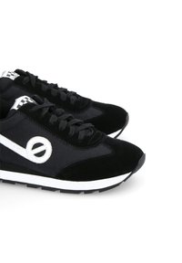 Black sneakers made of suede with smooth fabric panels, white accents, a distinctive logo, and a contrasting white midsole.
