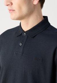 Tamsiai mėlynas polo marškinėliai pagaminti iš medvilnės, su apykakle su tekstūruotomis detalėmis, dviem juodais mygtukais ir įspaustu "BOSS" logotipu ant krūtinės.