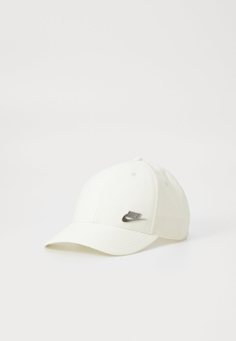 Bela bejzbol kapa iz tkanine, z izšito površino in kovinskim logotipom Nike spredaj. Enostaven dizajn brez vzorcev.