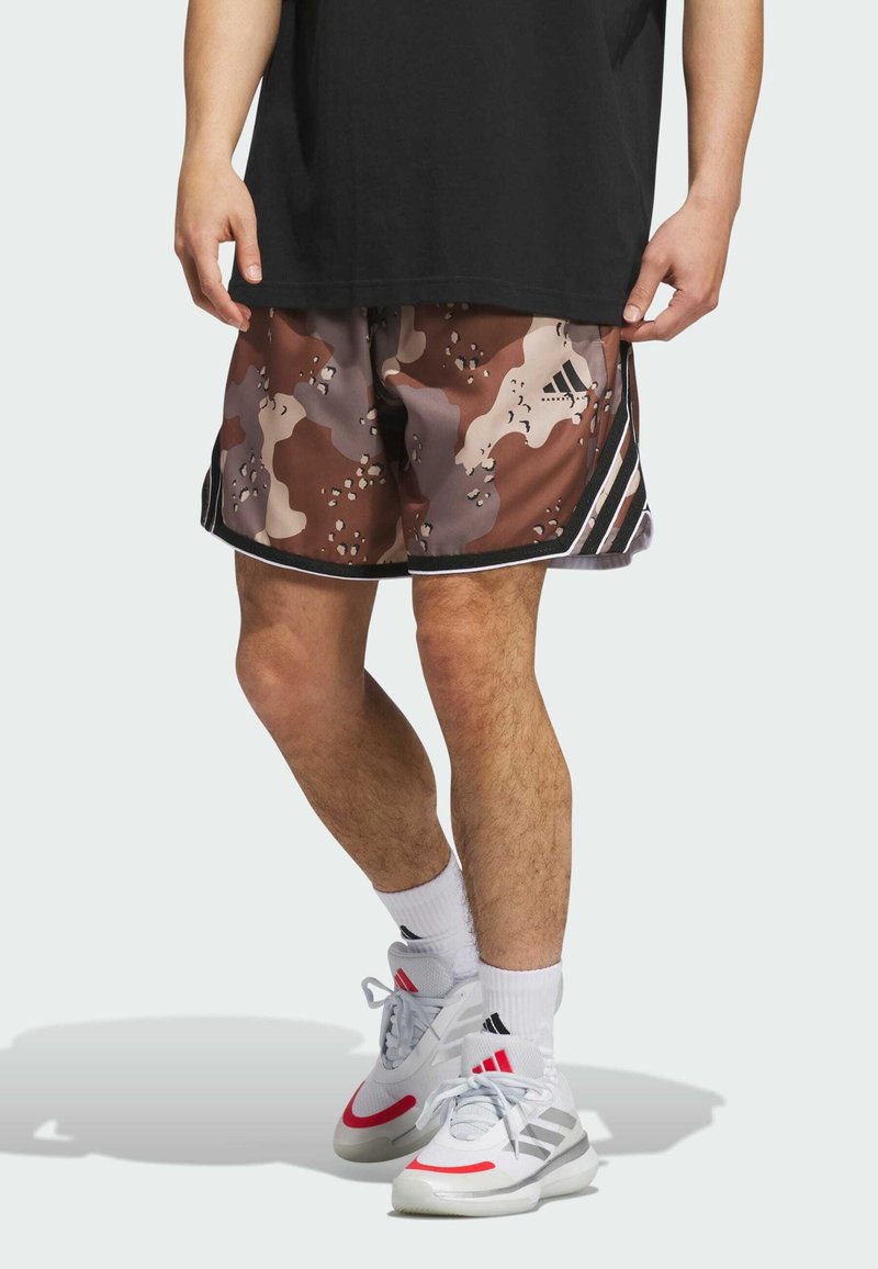 Herre brune camouflage shorts med lyse og mørke pletter, sorte sidestreger og en sort talje, iført hvide og røde sneakers.