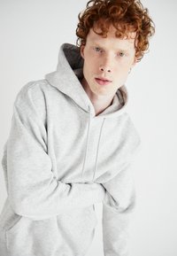 Sweat à capuche gris avec cordon de serrage, texture douce et coupe ample. Doté d'une poche kangourou et de poignets côtelés. Design uni, sans motifs.