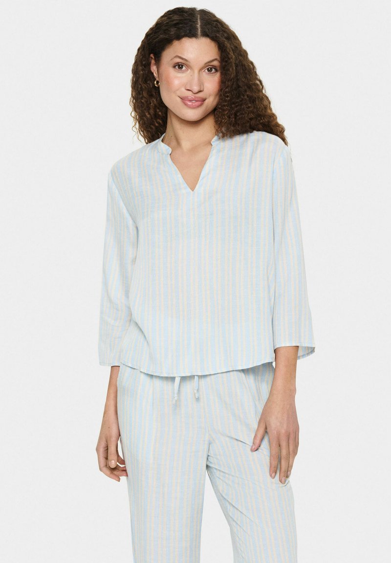 Top a righe blu chiaro e giallo con scollo a V e maniche a tre quarti, realizzato in un morbido tessuto texturizzato. Abbinato a pantaloni coordinati.