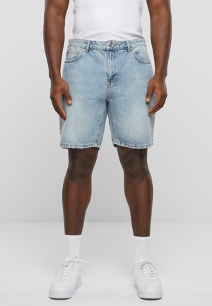 Shorts en denim bleu clair avec hems retroussés, design à cinq poches et une texture légèrement décolorée. Portés avec des baskets blanches et des chaussettes blanches à la cheville.