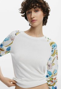 Maglione bianco con maniche a fantasia floreale colorata. Collo e polsini a costine. Design aderente con materiale morbido e leggero.