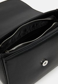 Svart strukturerad läderhandväska med flera zippered fack och ett silverfärgat tryckknappslås. Slät foder och elegant design.