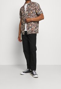 Kortärmad skjorta med flerfärgat paisleymönster; svarta byxor; svartvita sneakers; bomullstyg; ledig passform.