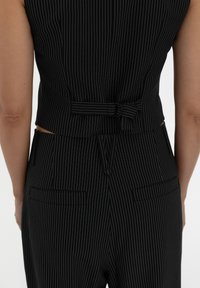 Black pinstriped two-piece outfit featuring a fitted top with a back bow detail and tailored trousers with back pockets.