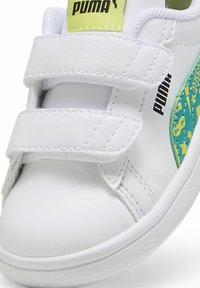 Baskets blanches avec deux bandes Velcro, présentant un accent texturé vert et jaune avec des étoiles. Logo Puma imprimé en noir sur le côté.