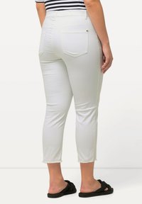 Pantaloni bianchi a vita alta con una texture liscia, dotati di tasche posteriori e orlo sfilacciato. Abbinati a scarpe nere in tessuto intrecciato da indossare senza lacci.