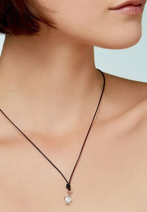 Close-up of a person’s neck and collarbone wearing a thin black cord necklace with a small turtle-shaped pendant.