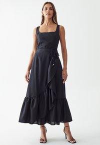 Black linen dress with a square neckline, tied waist, and a ruffled hem. Features a long, flowing design and subtle texture.