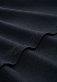 Donkerblauwe stof met een gladde textuur, met zachte plooien en subtiele breipatronen overal. Het materiaal lijkt lichtgewicht en flexibel te zijn.