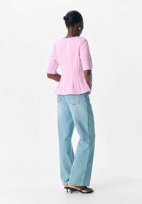 Rosa bomullstopp med korta ärmar och peplumdesign, i kombination med ljusblå hög midja jeans och svarta klacksandaler.