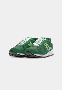 Et par grønne og lysegrønne atletiske sneakers med hvite snørebånd og polstrede hvite mellomsåler på en ensfarget bakgrunn.