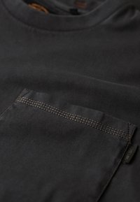 Zwarte katoenen T-shirt met ronde hals, voorzien van een zak met contrasterende bruin stiksel en een label aan de zijkant.