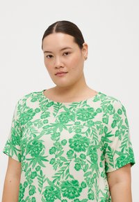 Grön blommönstrad topp med korta ärmar, rund halsringning och slät tygtextur på en ljus bakgrund.
