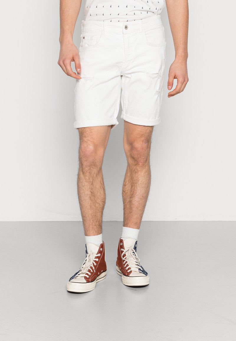 Shorts de mezclilla blanca con dobladillos enrollados, que presentan un ligero patrón desgastado. Combinados con zapatillas altas marrones y marinas.