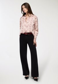 Camicia rosa chiaro con motivo scuro, maniche lunghe e colletto. Abbinata a jeans neri a vita alta e ampia e una cintura rossa. Scarpe nere a punta.