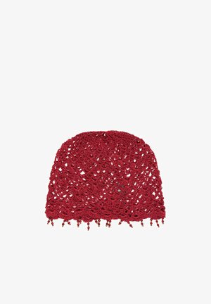 Bonnet rouge crocheté avec motifs floraux et petits détails perlés suspendus au bord sur fond blanc.