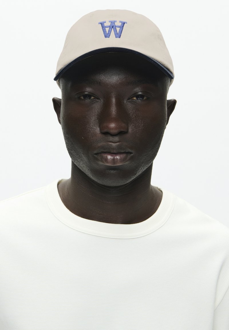 Light beige cap with a blue "W" logo, paired with a textured white long-sleeve shirt. Simple design, no additional accents or patterns.