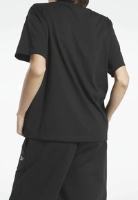 Svart bomull t-shirt med korta ärmar, avslappnad passform, rund halsringning och rak fåll. Visad bakifrån med avslappnade byxor.