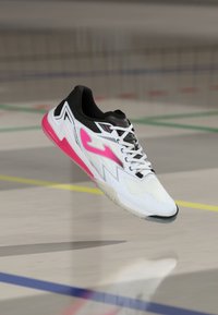 White athletic shoe with pink accents, black details, mesh upper, and a textured sole. Features bold design elements and lacing system.
