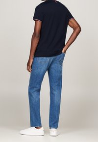 Navy short-sleeve polo with red and white collar trim, paired with light blue straight-leg jeans and white sneakers. Back view.