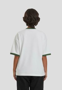 Camiseta blanca de gran tamaño con puños y collar verdes. Mangas cortas, tela suave, corte holgado y un diseño liso en la parte trasera.