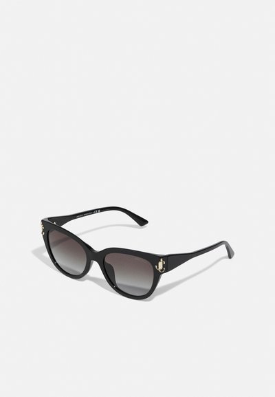 Des lunettes de soleil noires en forme d'œil de chat avec des verres dégradés, des accents en métal doré et une monture en plastique lisse. Logo notable sur les branches.