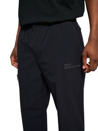 Sorte afslappede bukser med elastisk talje og subtil "HALO 19681972981" tekst på højre lår, båret med en sort skjorte.