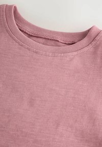 Helles rosa T-Shirt mit rundem Ausschnitt, aus strukturierter Baumwollqualität gefertigt und mit dezenten Nähten entlang der Kanten.