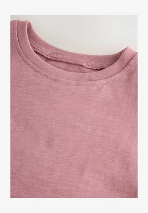 Világos rózsaszín T-shirt, kerek nyakkivágással, amit textúrált pamutanyag jellemez, finom varrásokkal az élein.