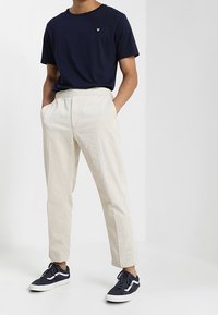 Námořnická bavlněná tričko s malým logem, spárované s krémovými texturovanými tapered kalhotami a námořnickými teniskami s bílou podrážkou.