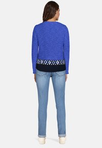 Pull bleu texturé avec un ourlet à motif marine, assorti à un jean en denim bleu clair et des baskets blanches, vu de dos.