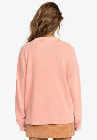 Übergroßer rosa Sweatshirt mit strukturiertem Strickmuster, langen Ärmeln und überschnittenen Schultern, kombiniert mit einem beigen Cord-Rock.