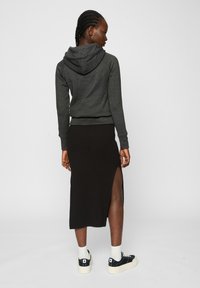 Sudadera gris oscuro con capucha, combinada con una falda negra de gran abertura y zapatillas negras con suelas blancas. Tejido suave; estilo casual.