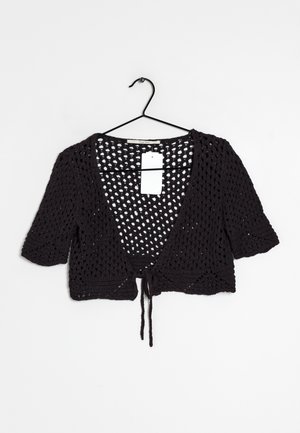 Cardigan court en crochet noir à manches courtes, devant ouvert avec fermeture à nouer, suspendu sur un cintre en fil métallique noir sur fond blanc.