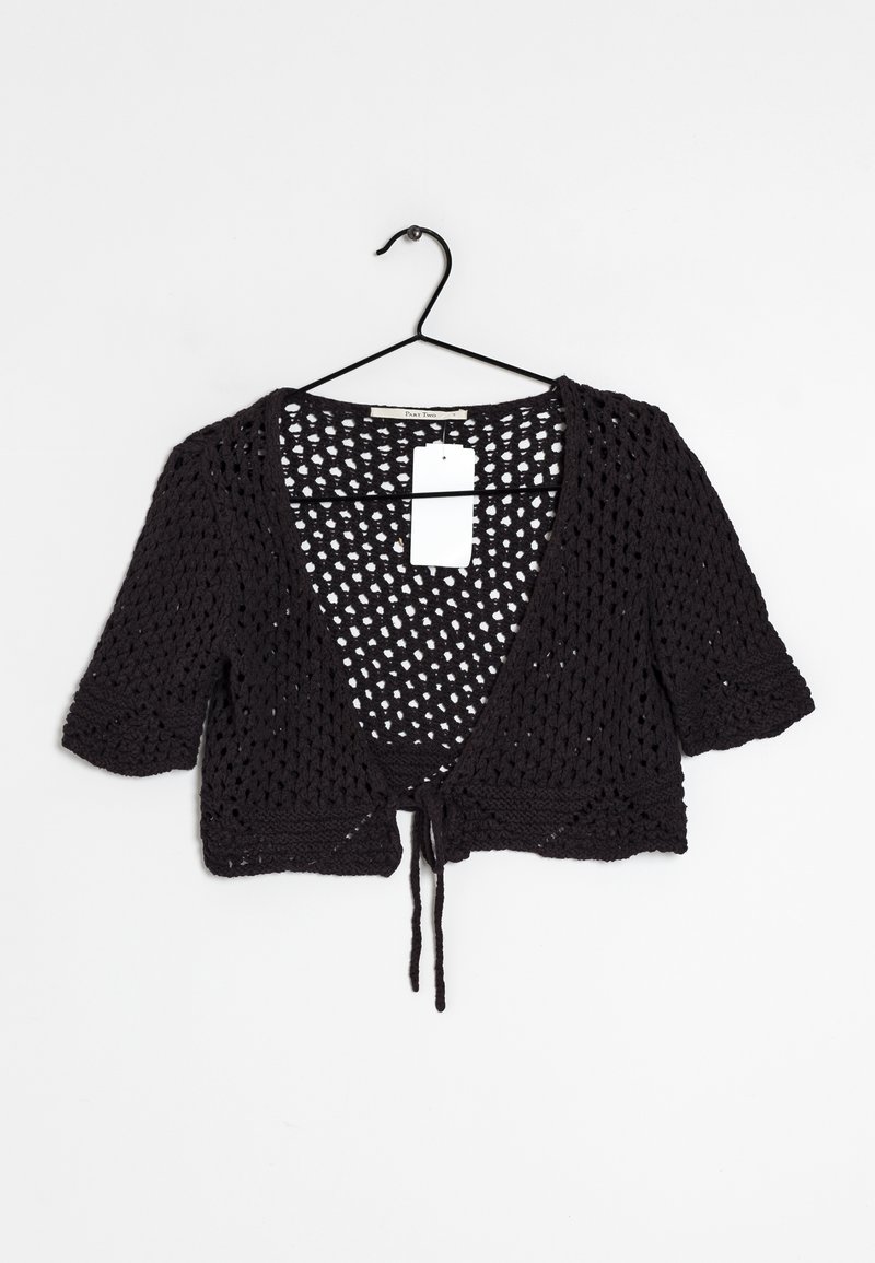 Cardigan court en crochet noir à manches courtes, devant ouvert avec fermeture à nouer, suspendu sur un cintre en fil métallique noir sur fond blanc.