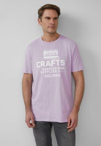 Lila katoenen T-shirt met een witte grafische print met de tekst "KUNST- EN HANDWERKSERVICE EN MATERIALEN". Korte mouwen en een ronde halsontwerp.