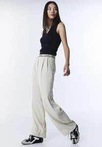 Top negro sin mangas, pantalones anchos crema plisados con una cintura de marca y zapatillas negras con detalles texturizados y acentos blancos.