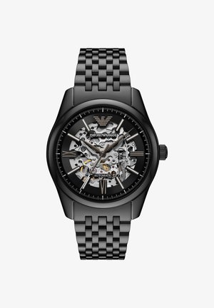 Reloj automático de metal negro con engranajes plateados expuestos, números romanos y marcas horarias de barra, y pulsera enlazada.